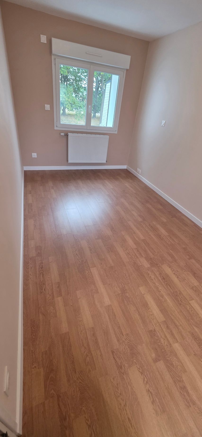 Une pièce vide avec un parquet et une fenêtre laissant entrer la lumière du jour.