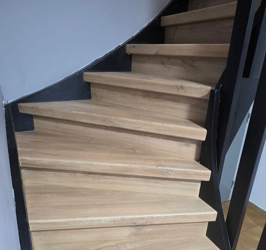 Un escalier en bois courbé avec des rampes noires.