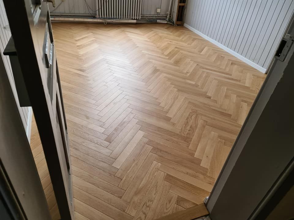Une pièce vide avec parquet clair à chevrons et un radiateur au mur.