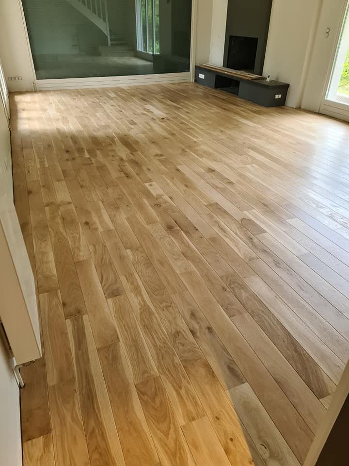 Une grande pièce vide et lumineuse avec un parquet en bois clair.