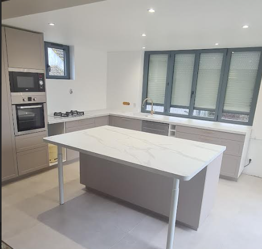 Cuisine blanche moderne avec un îlot central, un four encastré et une grande fenêtre.