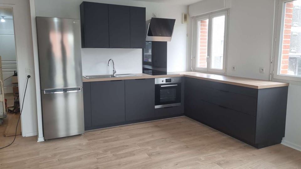 Une cuisine moderne avec des placards foncés, un réfrigérateur en inox et un parquet au sol.