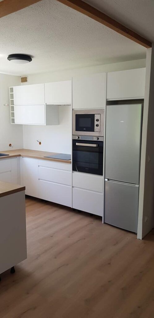 Une cuisine moderne blanche avec des placards en bois, un four encastré et un réfrigérateur en acier inoxydable.