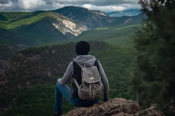 Persona con mochila mirando desde un acantilado un monte.