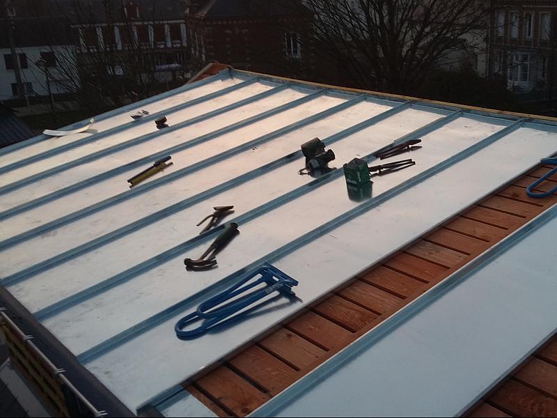 Toiture métallique avec outils, partiellement installée, surplombant les bâtiments par une journée ensoleillée.