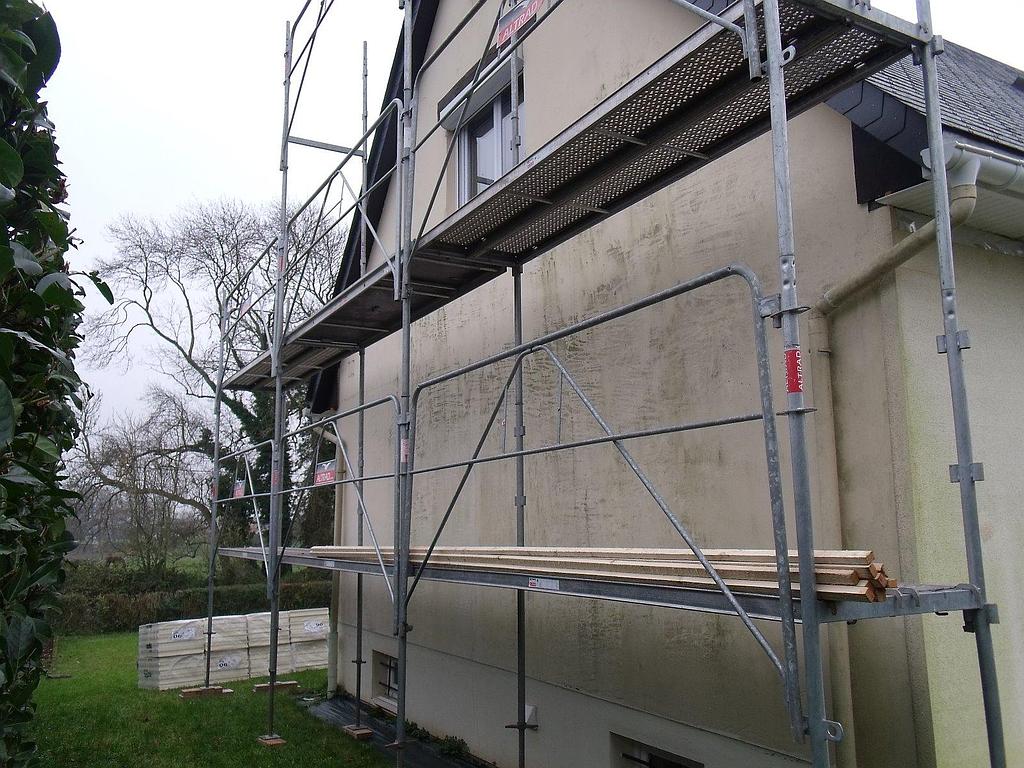 Échafaudage à côté d'une maison avec des algues visibles sur le mur extérieur ; cadre extérieur nuageux.