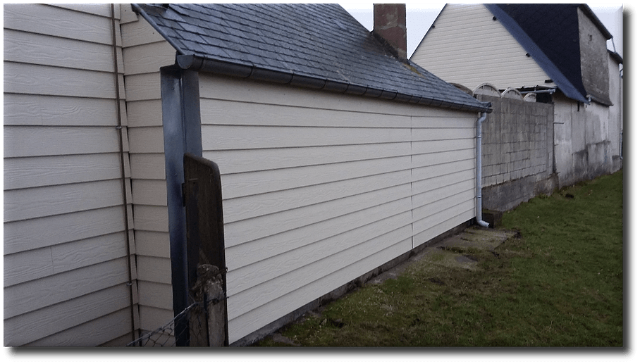 Revêtement beige sur un bâtiment bas au toit foncé, à côté d'un mur de béton et de gazon.