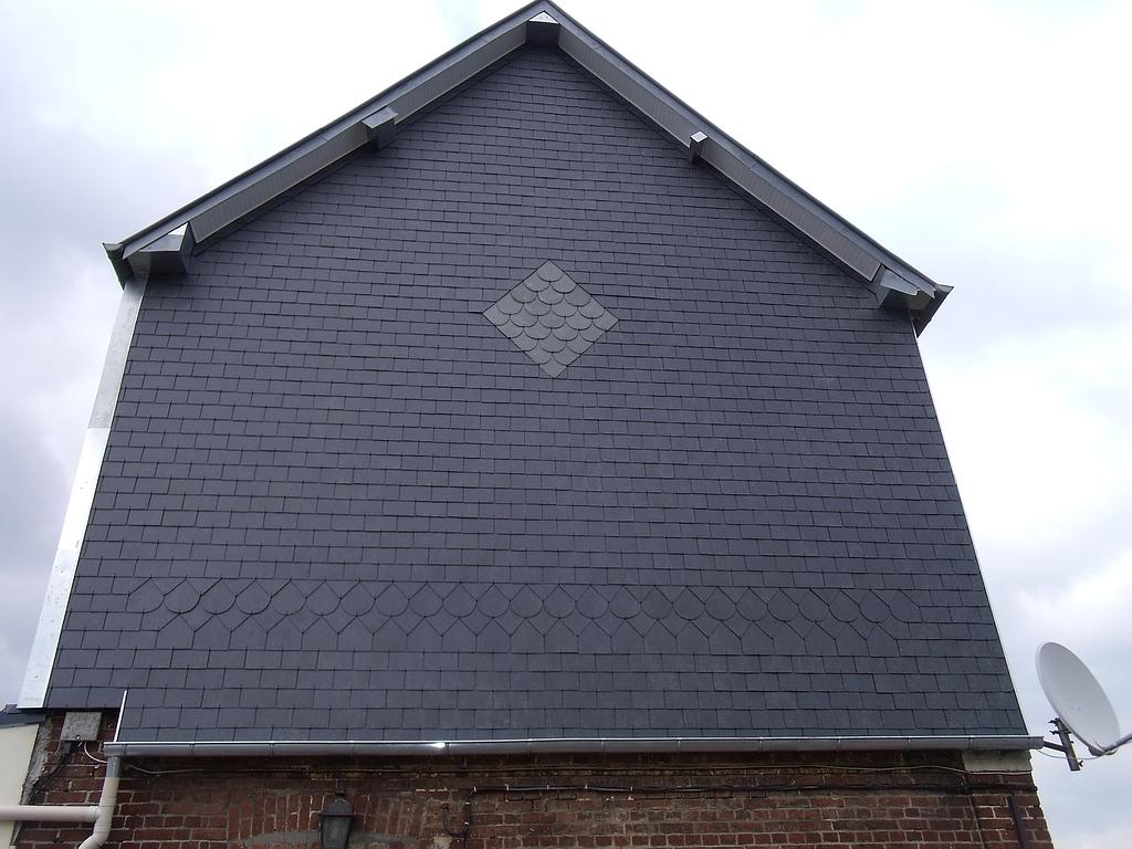 Toiture en ardoise gris foncé à motifs de losanges, adossée à un mur de briques. Une antenne parabolique y est fixée.