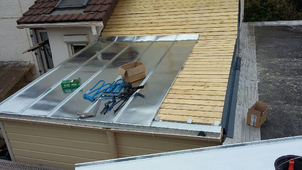 Travaux sur le toit d'un immeuble ; panneaux métalliques installés, charpente en bois visible. Outils et cartons éparpillés.
