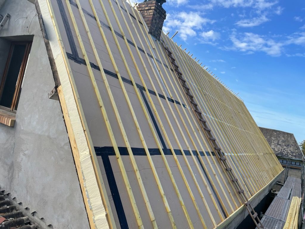 Rénovation de toiture : planches de bois avec ruban adhésif noir et jaune sur bâtiment avec fond de ciel bleu.