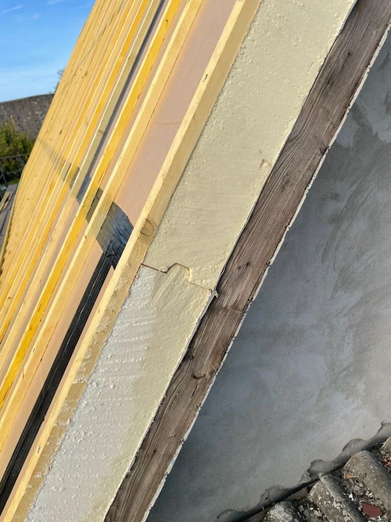 Gros plan des couches de construction : isolation jaune, mousse beige, garnitures en bois et stuc gris.