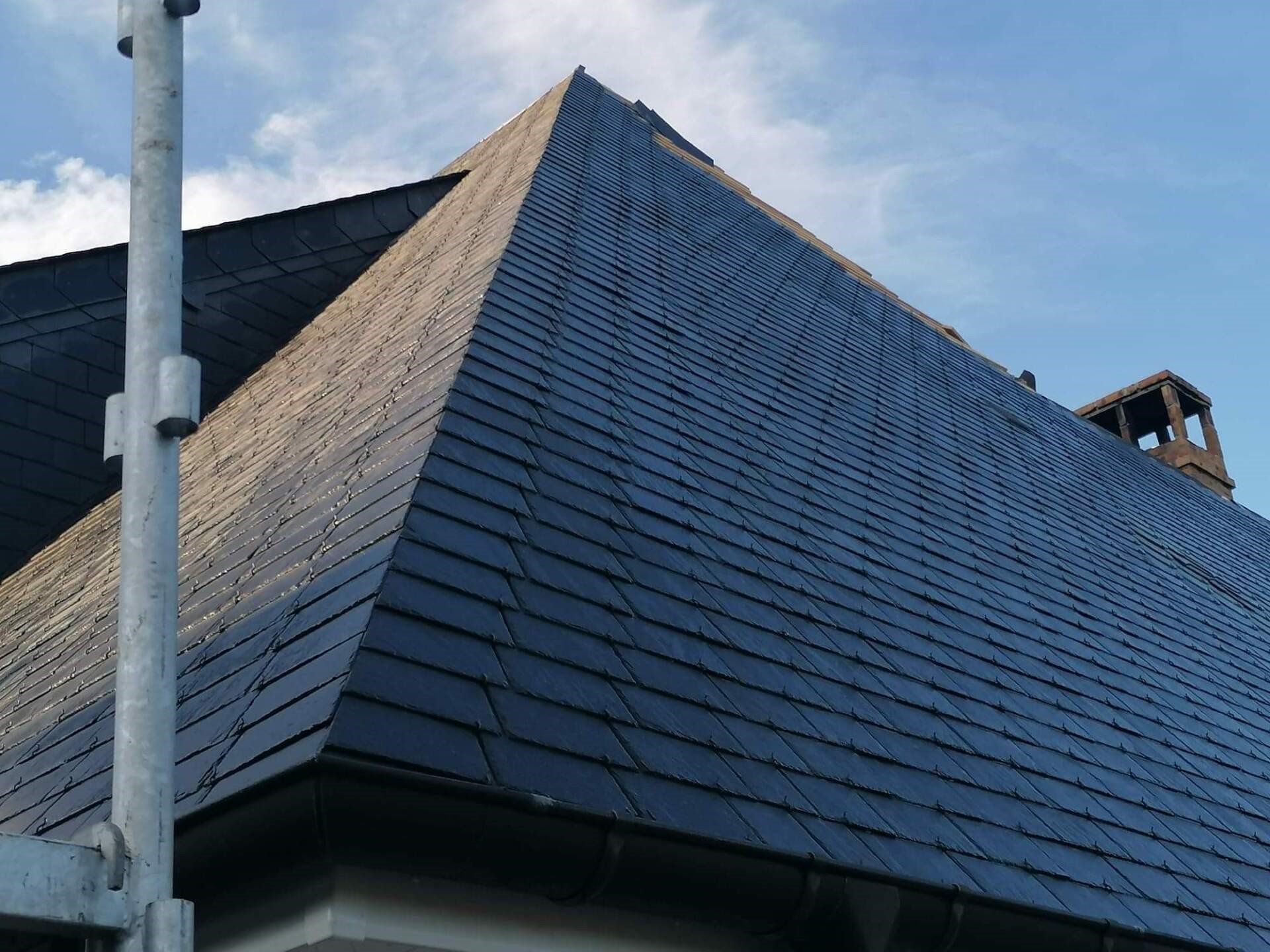 Toit en ardoise foncée d'un bâtiment sous un ciel bleu, avec un échafaudage au premier plan.