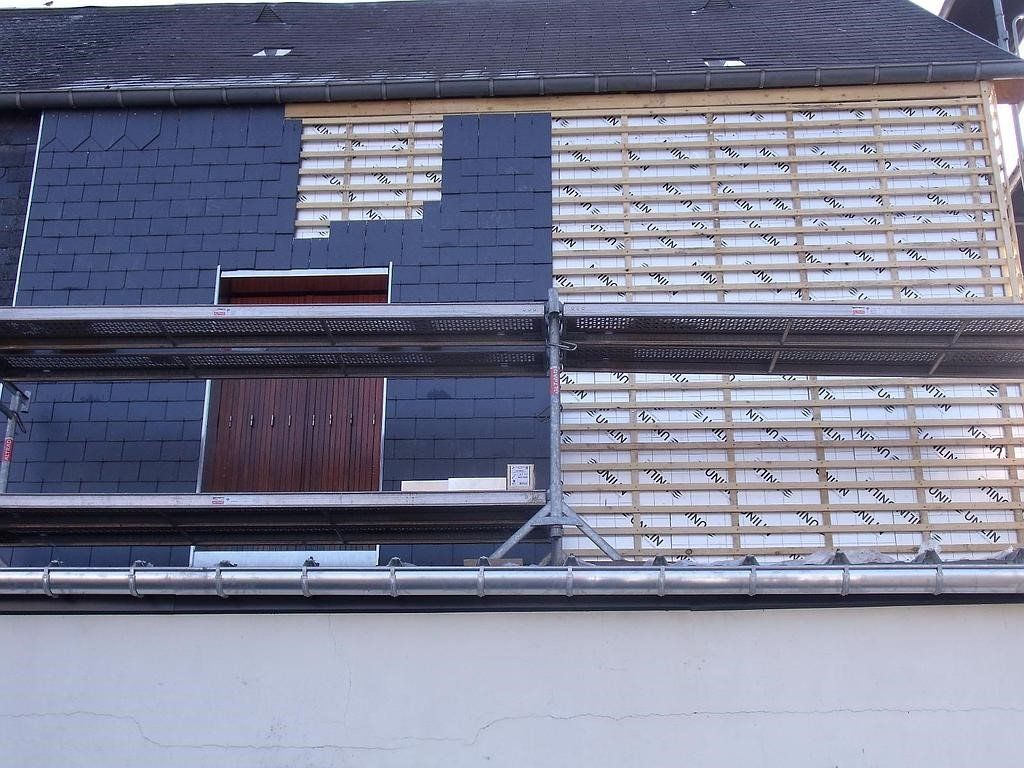 Toiture en cours de réparation, avec bardeaux d'ardoise foncée et charpente apparente. Échafaudage en place.