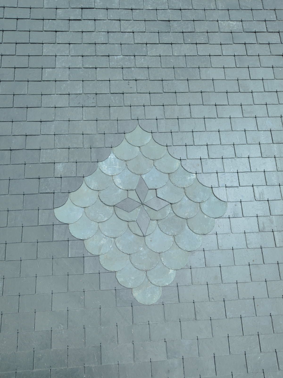 Toiture en ardoise grise à motif losangique en tuiles festonnées.