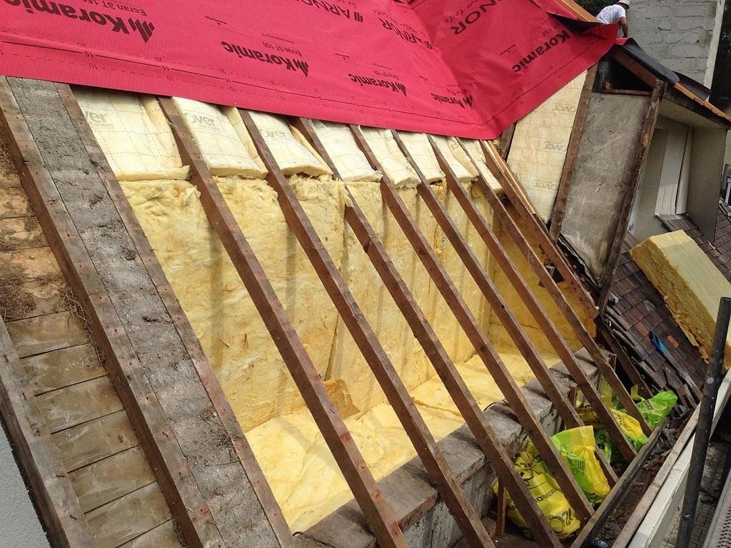 Pose d'isolation de toiture : isolation jaune entre chevrons, sous-couche rouge, extérieur.