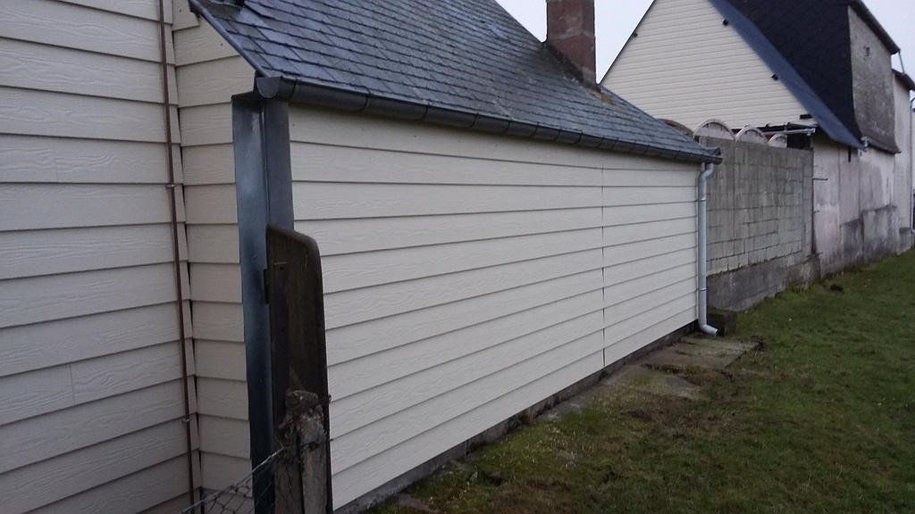 Revêtement beige sur un bâtiment, à côté d'une clôture en bois, situé dans un espace extérieur gazonné.