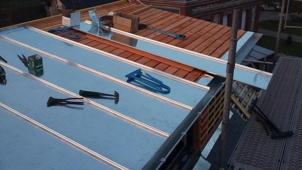 Pose d'une toiture métallique sur un bâtiment en construction ; les outils sont éparpillés sur la surface.