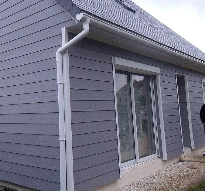 Maison grise avec boiseries, gouttières et bardage blancs. Une porte coulissante en verre est visible.