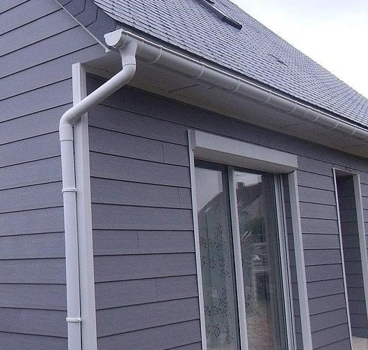 Revêtement gris sur un bâtiment avec des gouttières blanches, un tuyau de descente et une fenêtre.