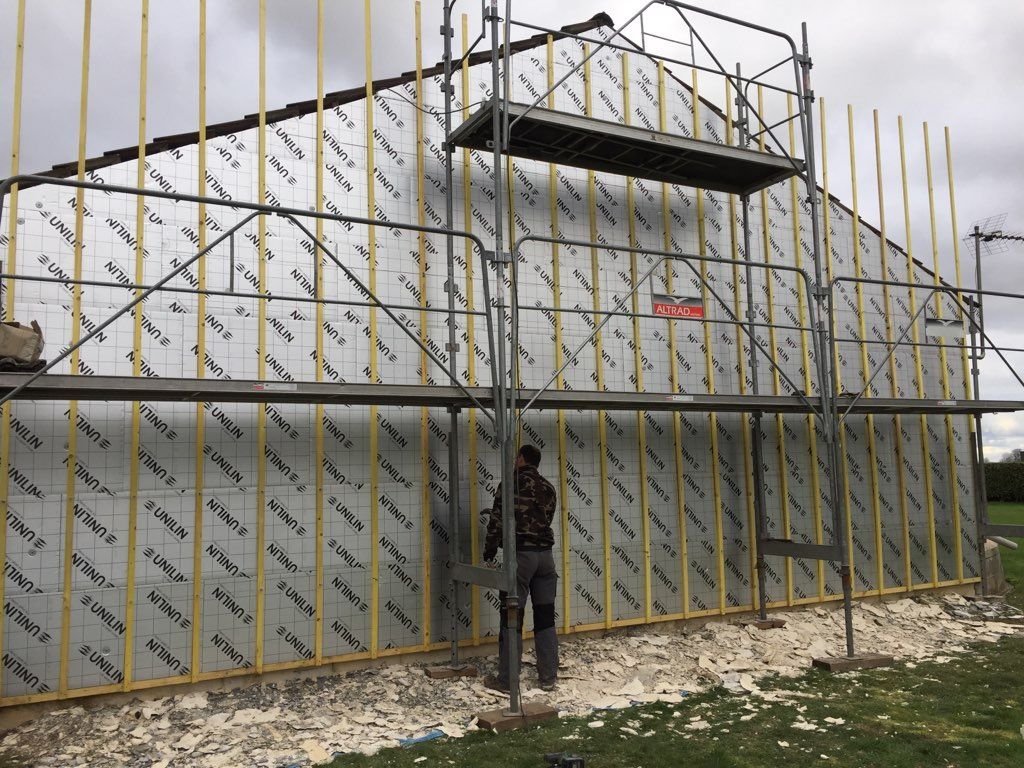 Un ouvrier du bâtiment installe l'isolation extérieure d'une maison à l'aide d'un échafaudage.