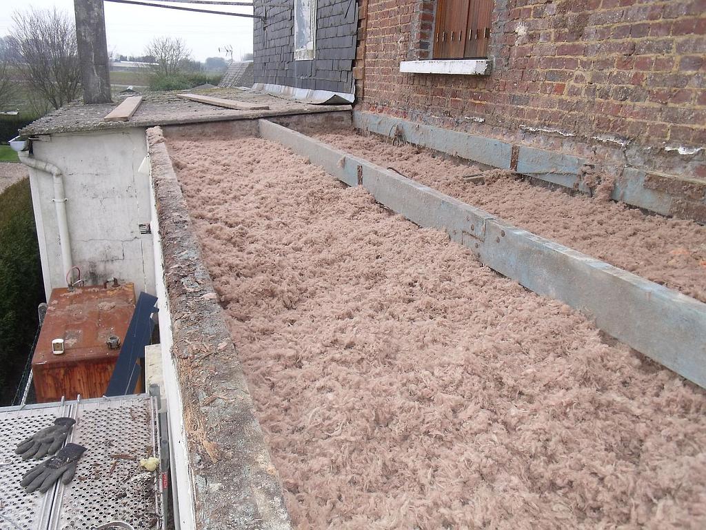 Toiture plate avec isolation brune entre barrières de béton, à côté d'un mur de briques.