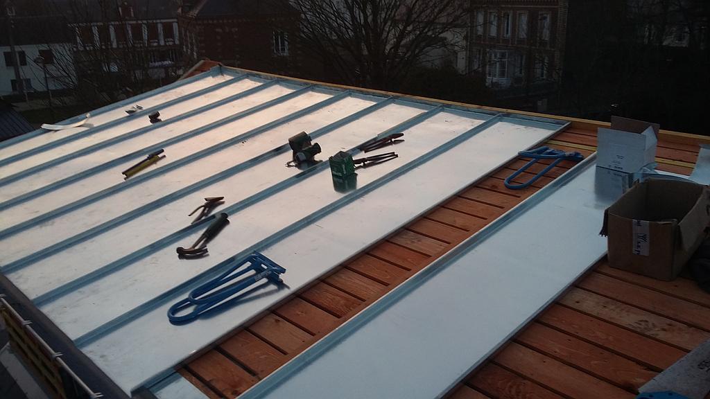 Pose de toiture métallique avec outils et matériaux sur un bâtiment, ensoleillement, environnement extérieur.