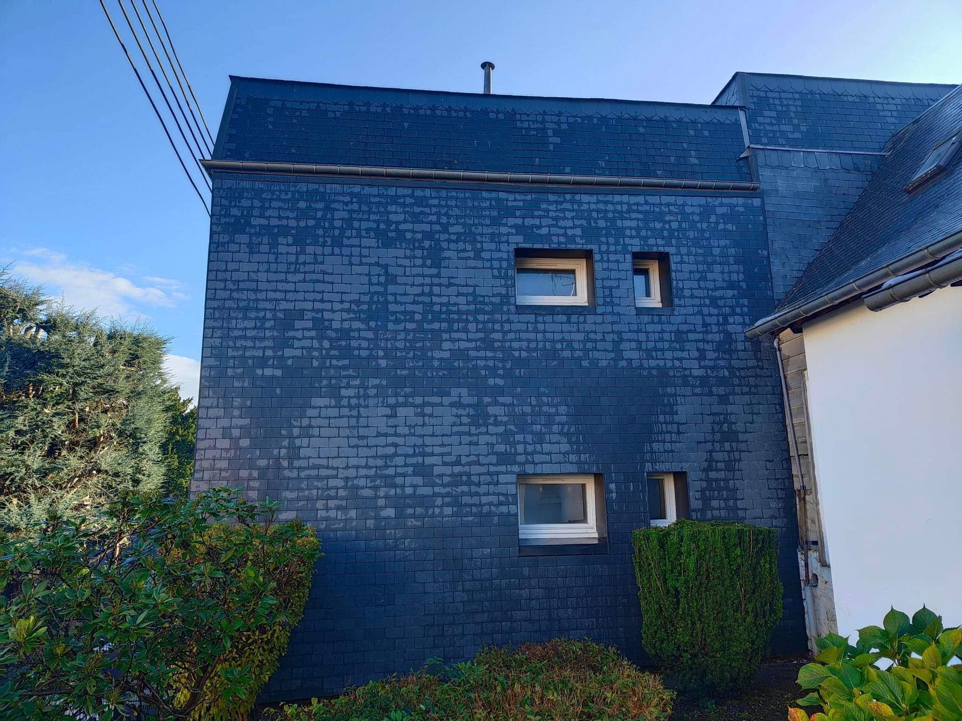 Bâtiment bleu foncé recouvert d'ardoises, avec des fenêtres à cadre blanc sur fond de ciel bleu.