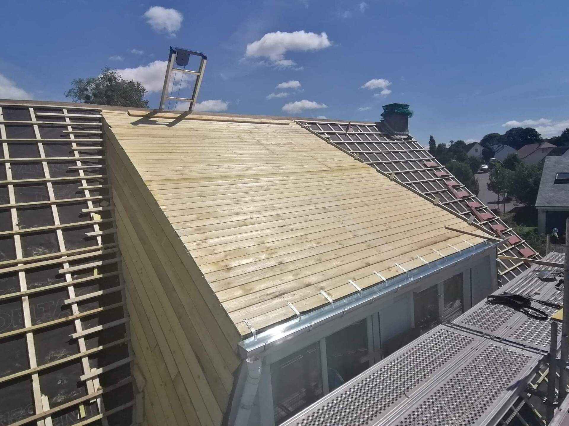 Construction du toit : Planches de bois posées sur un toit partiellement fini avec échafaudage.