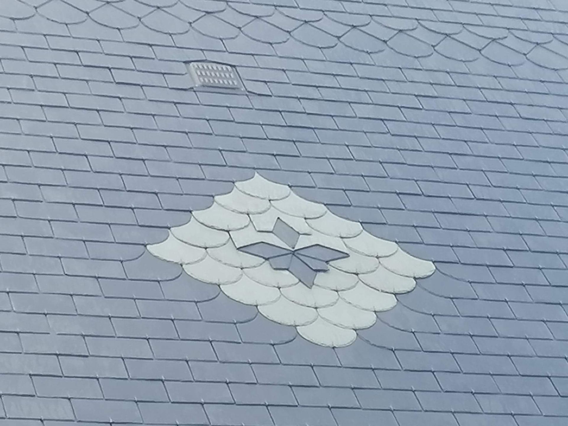 Toiture en ardoise avec motif décoratif en losanges et étoiles de couleur claire.