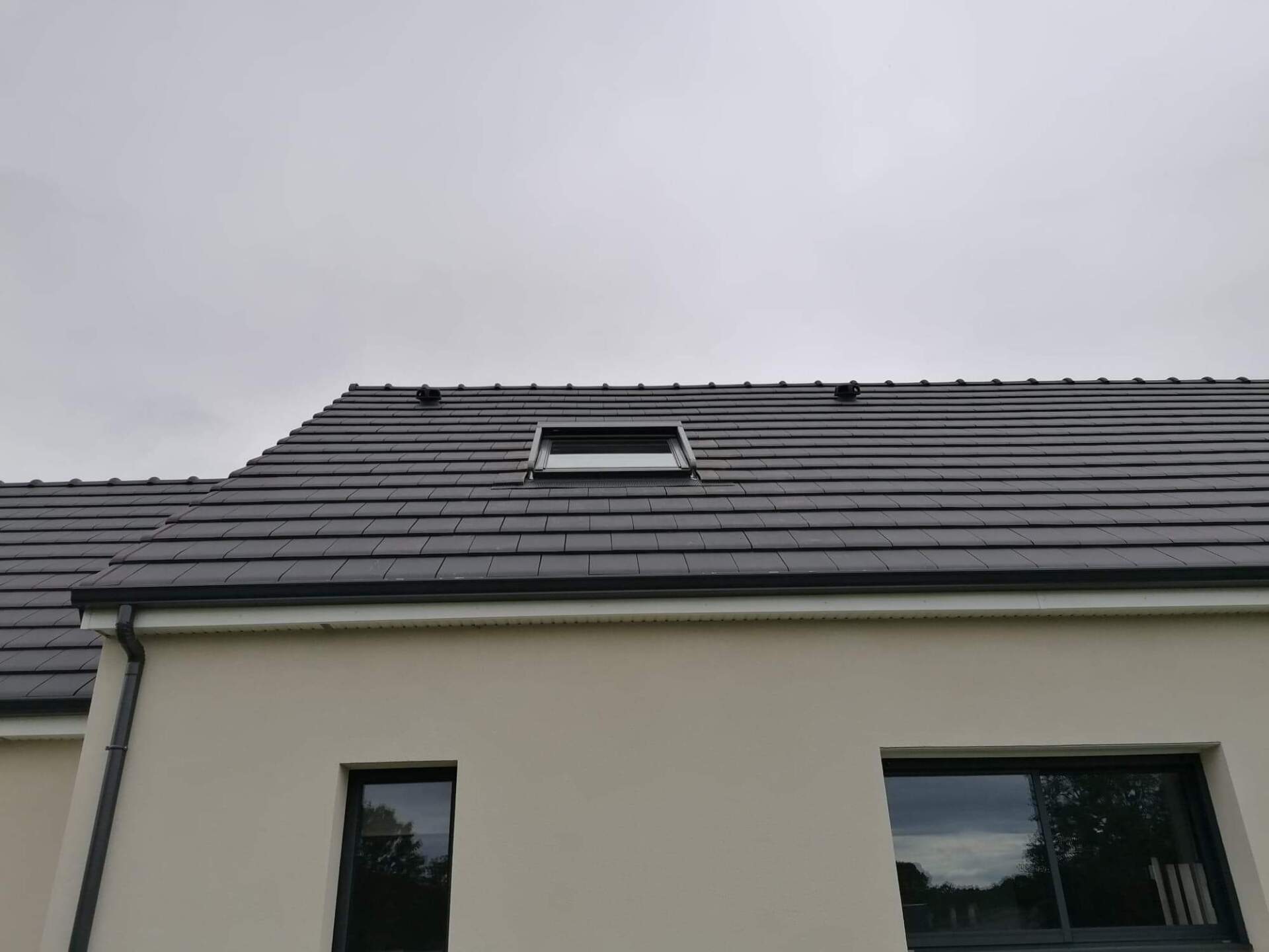 Une maison avec un toit de tuiles grises et une lucarne par temps nuageux.