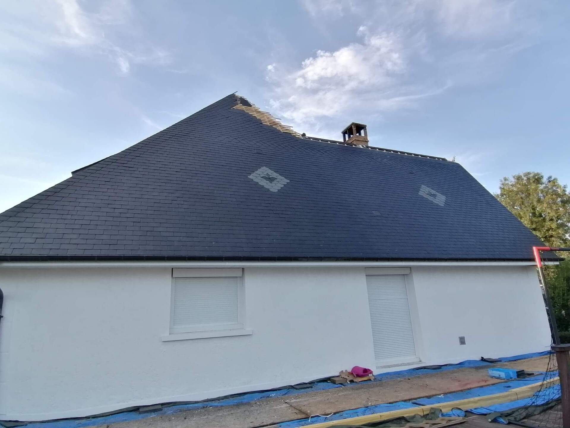 Maison blanche au toit sombre et à la cheminée sur fond de ciel bleu. Deux volets fermés.