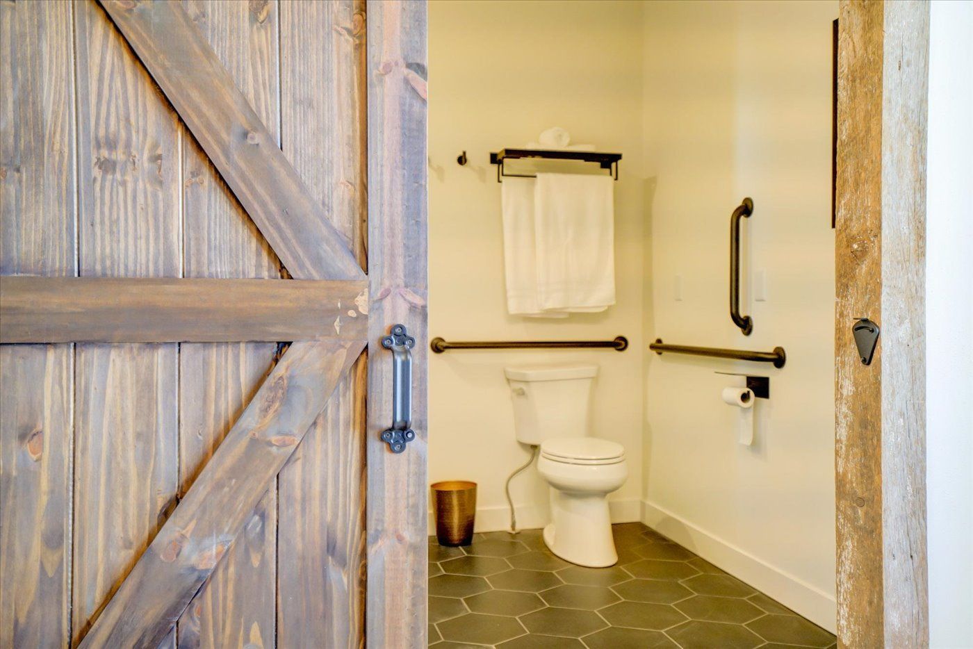 Barn door reveals accessible bathroom with grab bars and a toilet.