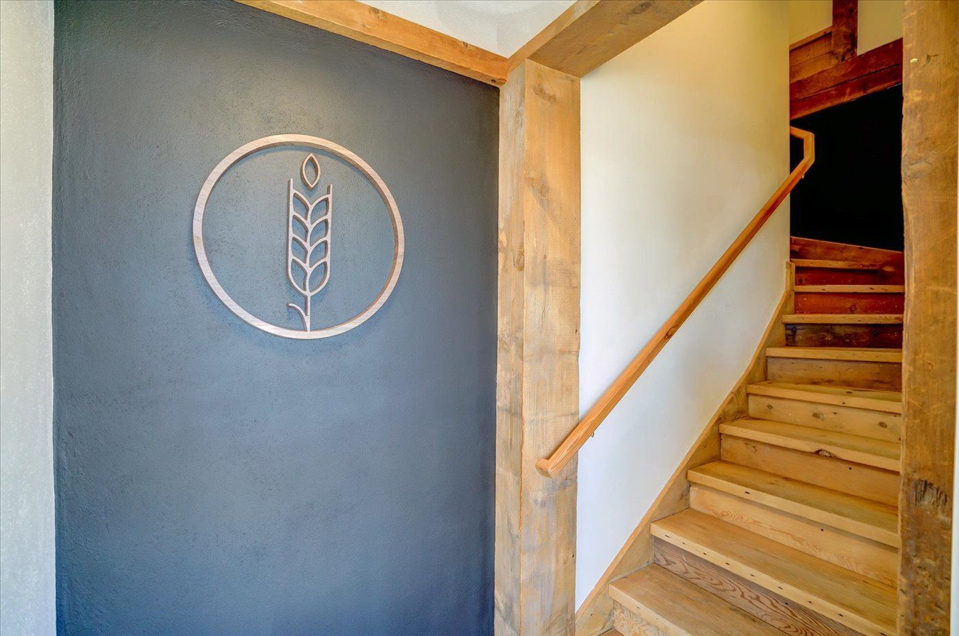 Entryway with a wooden staircase and a wheat stalk symbol on a dark gray wall.