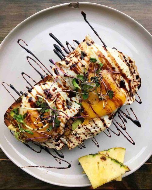 Toast topped with ricotta cheese, grilled pineapple, sprouts, and balsamic glaze on a white plate with pineapple slices.