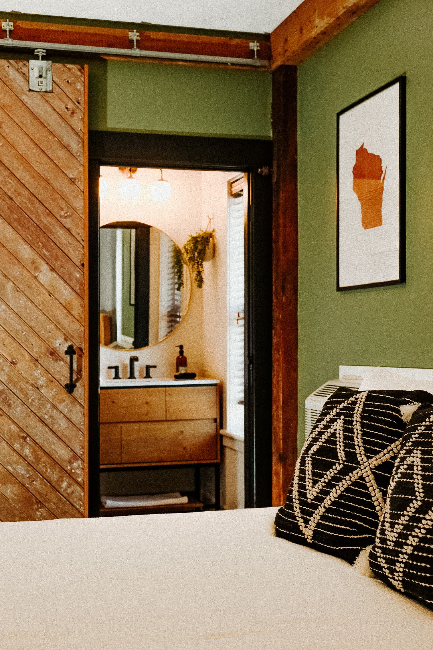Bedroom with barn door, opening to a bathroom. Olive green walls, wood accents, modern art.