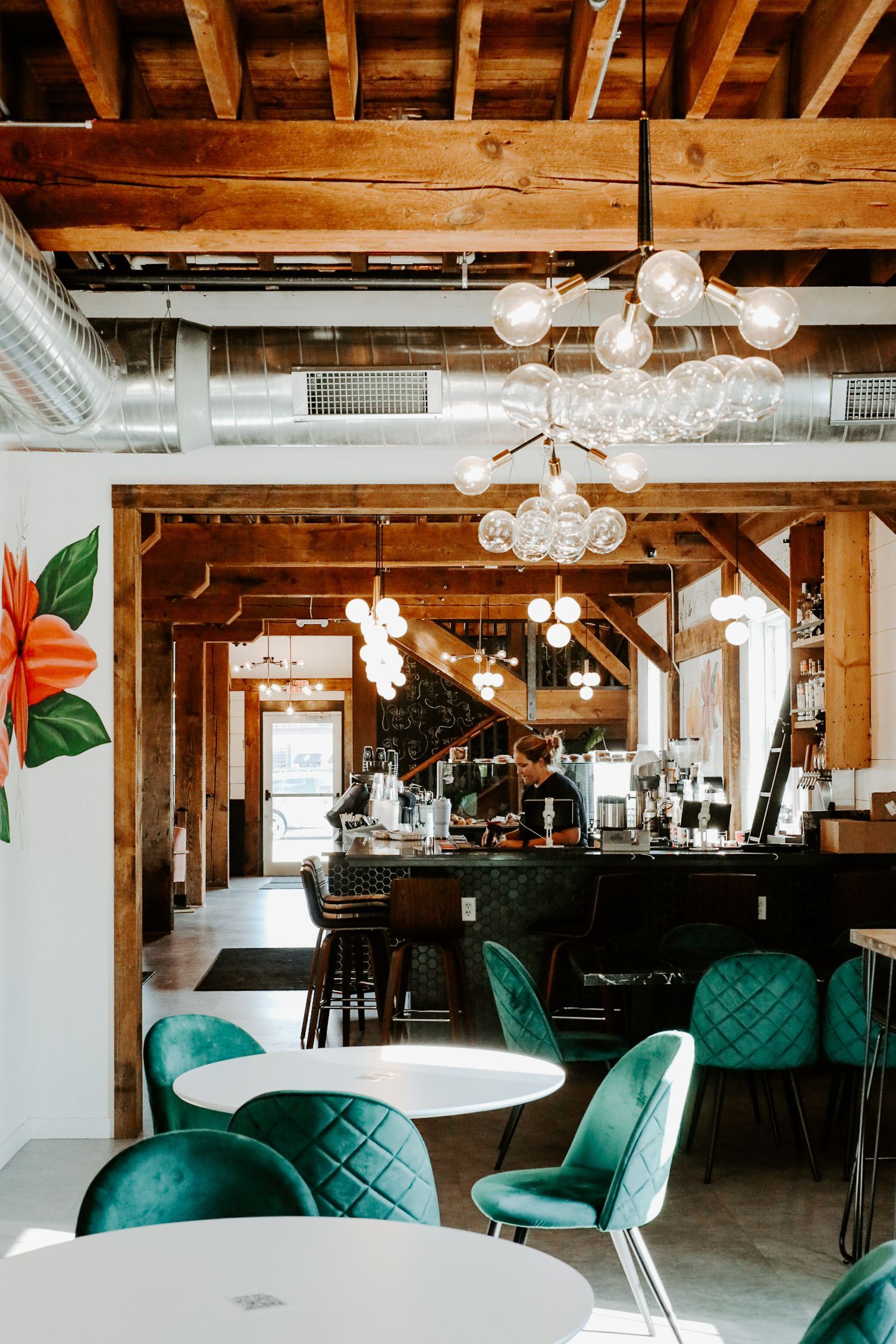 Interior of a cafe with teal chairs, white tables, wooden beams, and a bar in the background.