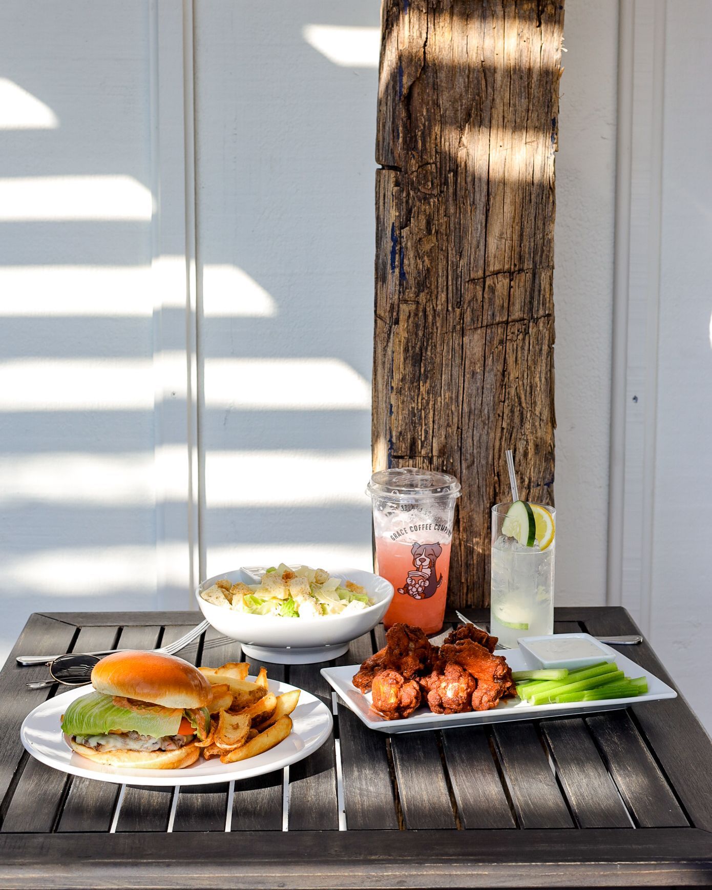 Lunch spread: burger, salad, chicken wings, and drinks on a table next to a wooden post.