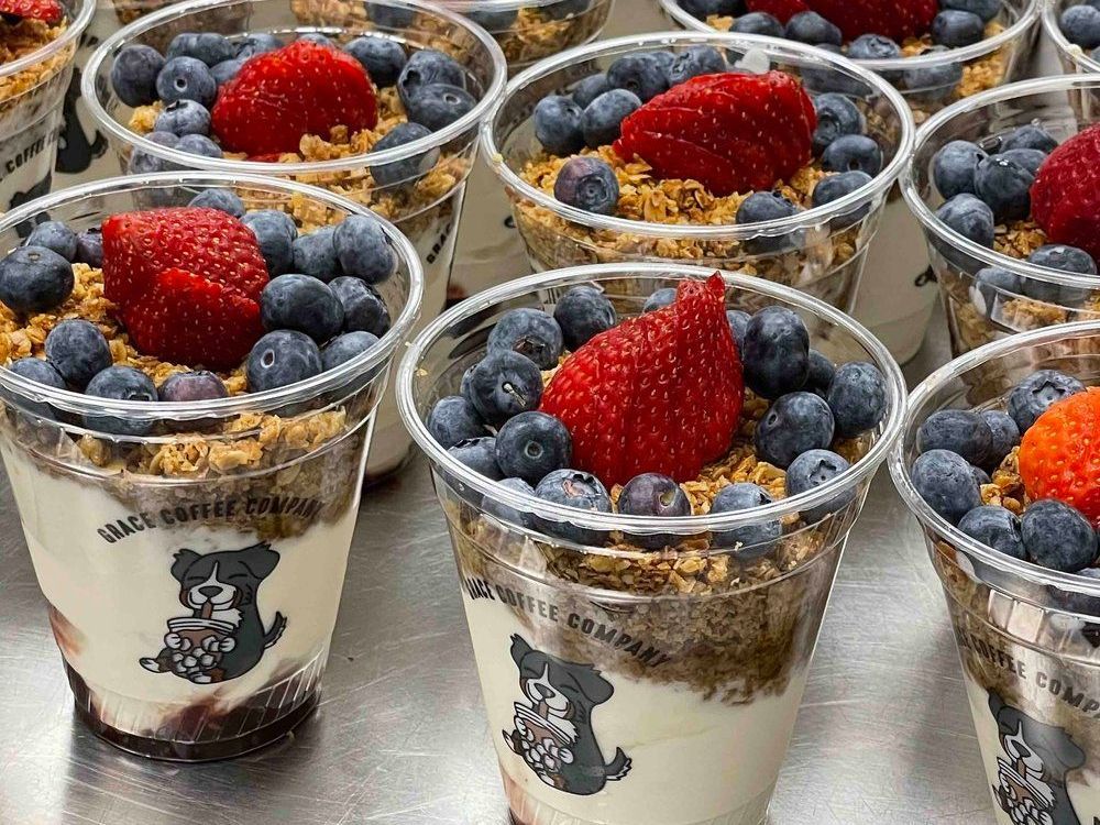 Cups of layered yogurt with granola, blueberries, and a strawberry.
