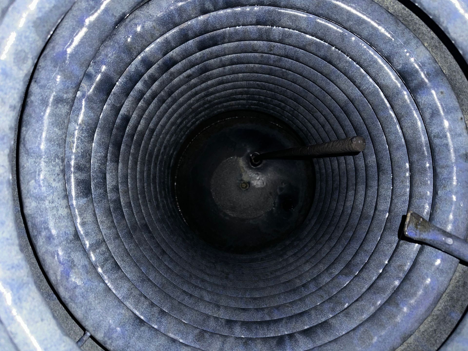 Blick in ein blaues Wellrohr oder einen Tunnel mit einer dunklen, kreisrunden Öffnung in der Mitte.