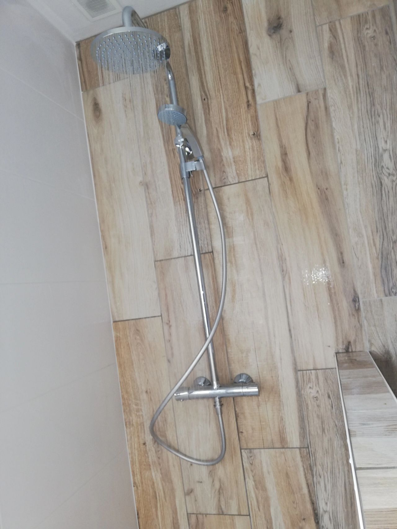 Ensemble de douche avec pommeau de douche à effet pluie et douchette à main sur mur en carrelage imitation bois.