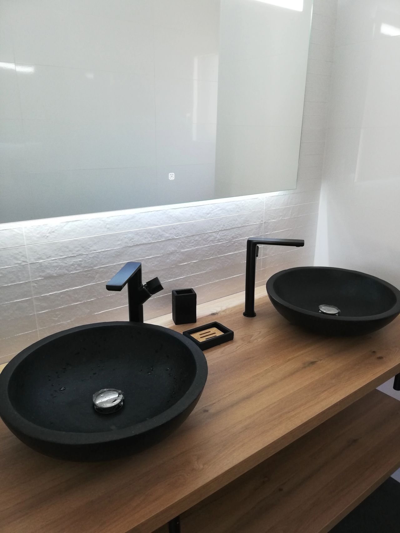 Deux vasques noires sur une vanité en bois avec robinets noirs, sous un grand miroir.