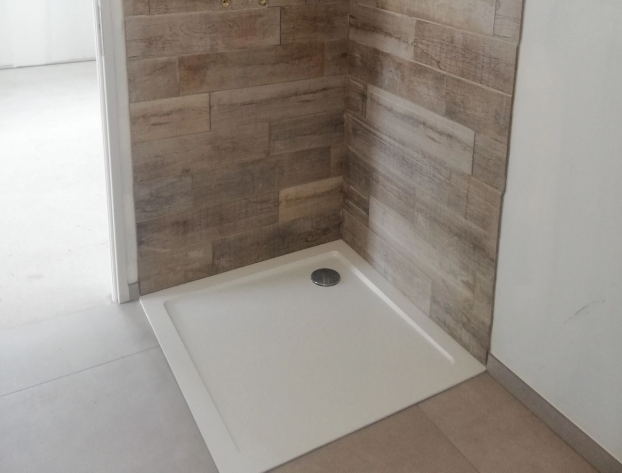Receveur de douche blanc installé, contre des murs carrelés imitation pierre, dans une pièce en construction.
