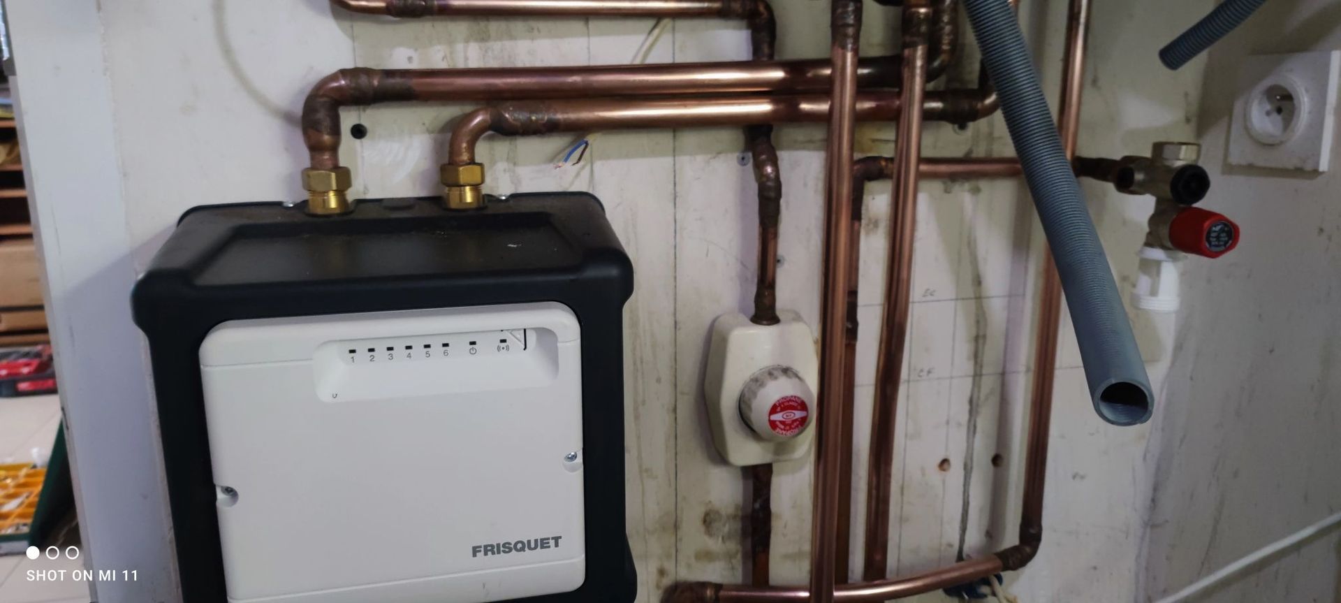 Tuyaux en cuivre et composants électriques installés sur un mur. Un panneau de commande blanc se trouve au centre.