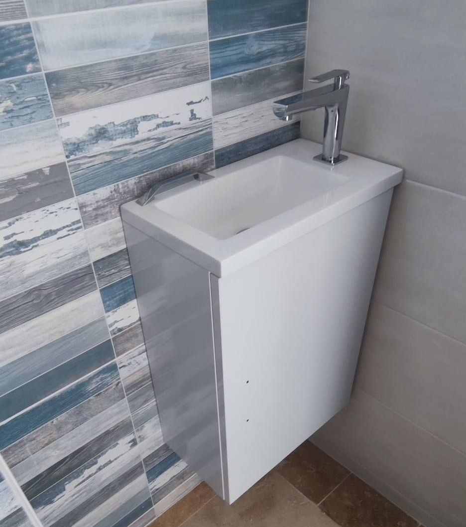 Lavabo mural blanc dans une salle de bain, avec robinet chromé. Carrelage mural à motifs bleu et gris.