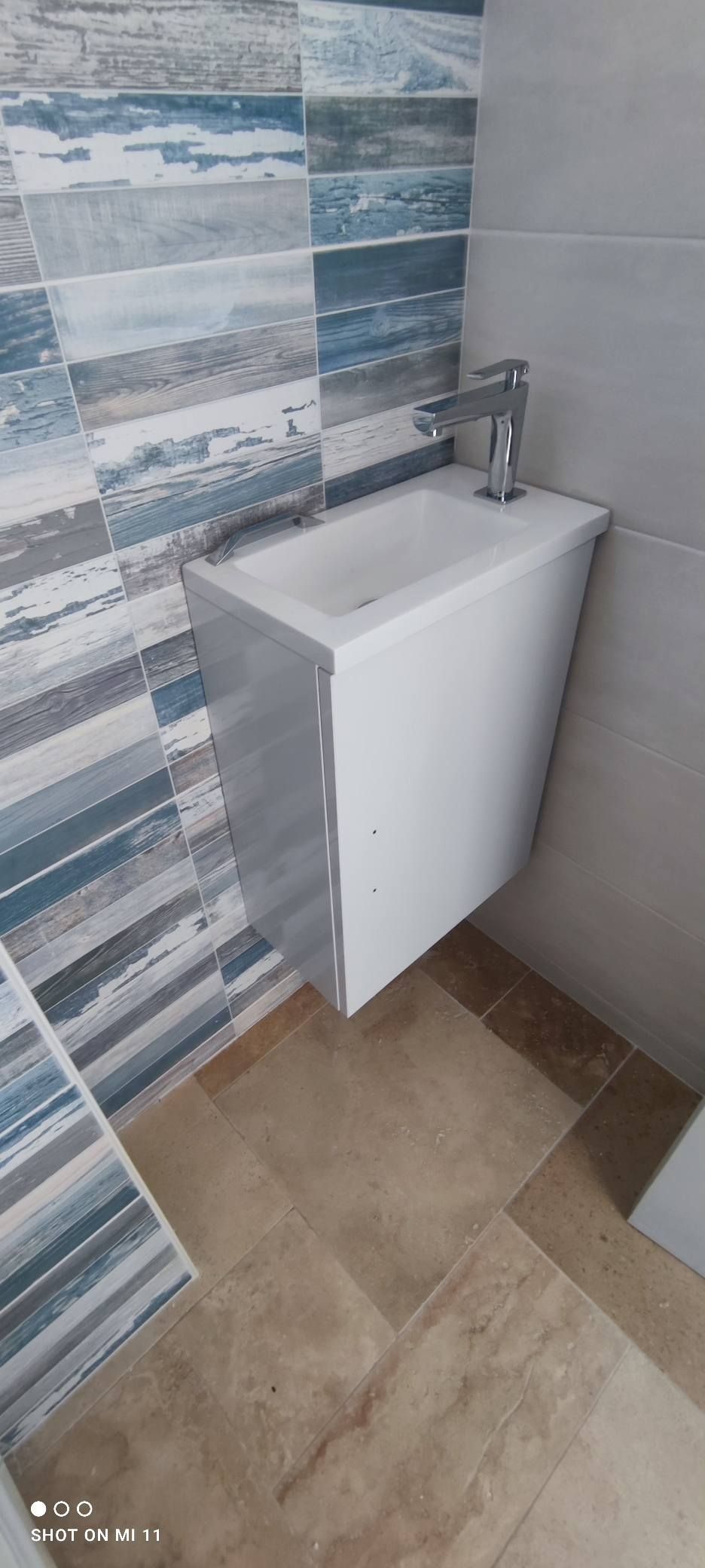 Un petit lavabo blanc avec un robinet chromé monté sur un mur de salle de bains avec des carreaux bleu et gris.