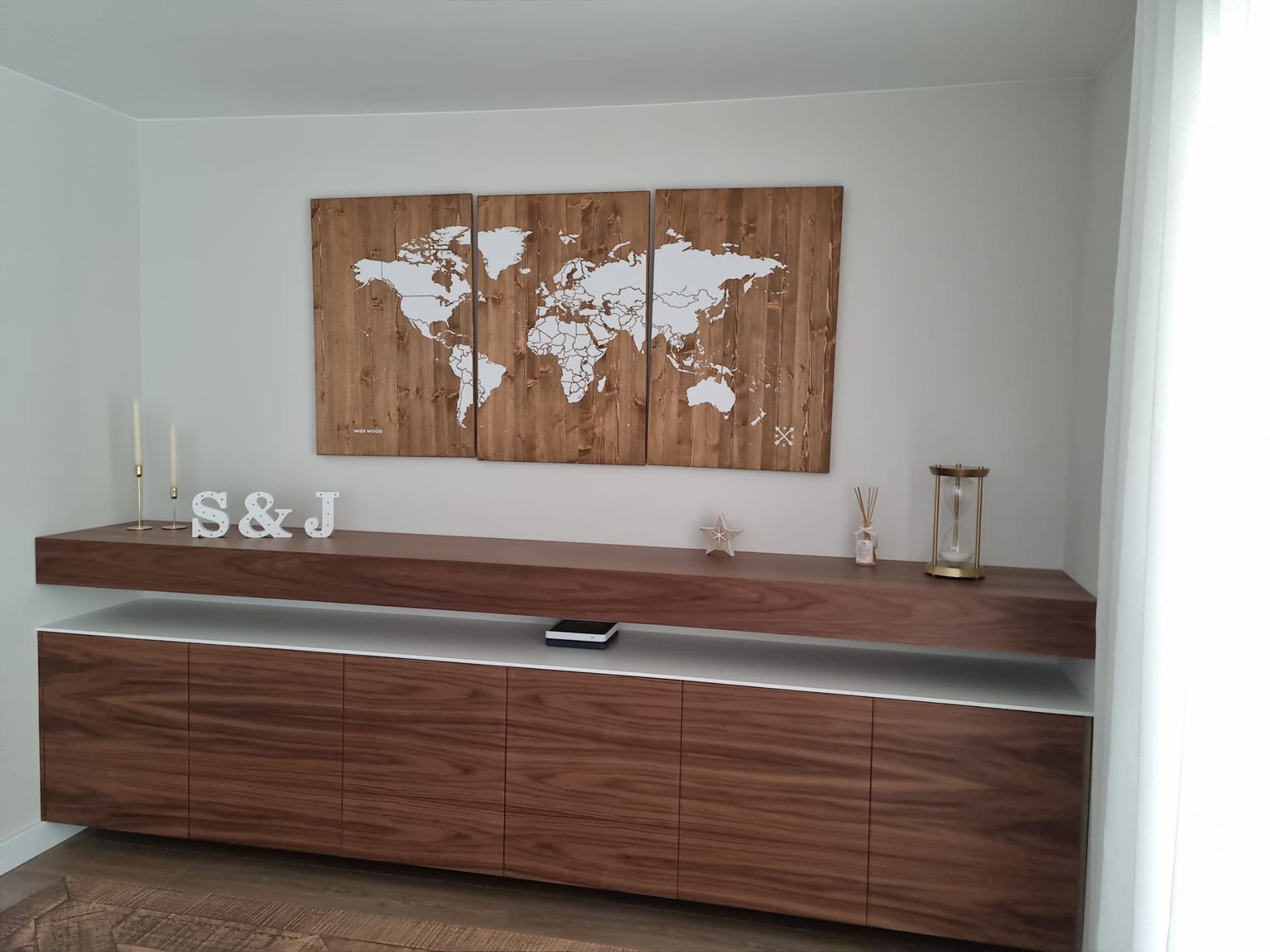 Un mapa de madera del mundo está colgado en una pared encima de un estante de madera.