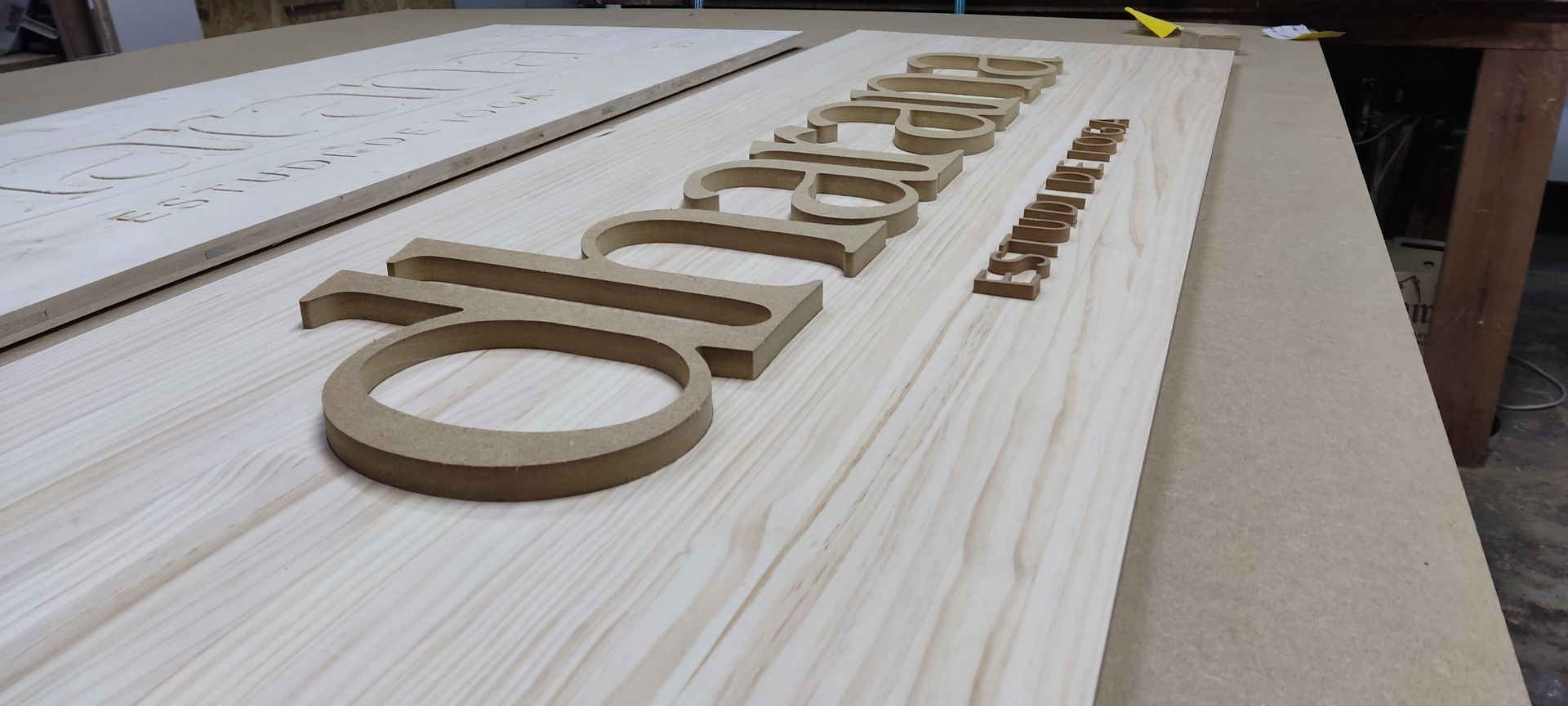 Letrero de madera con letras fresadas en un entorno de taller. El letrero dice 