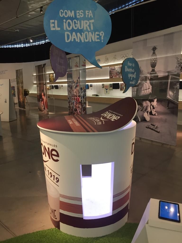 Una exhibición de un vaso de yogur con un cartel que dice com es fa el iogurt danone