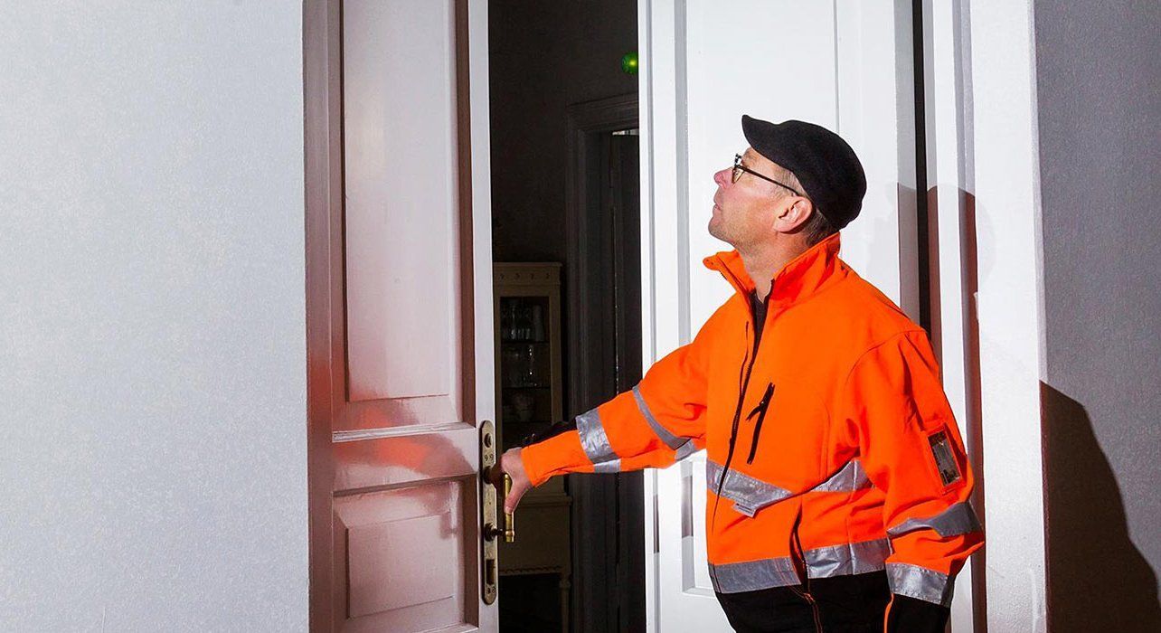 Oranssissa turvaliiveissä oleva työntekijä kurottaa ovenkahvaan sisätiloissa