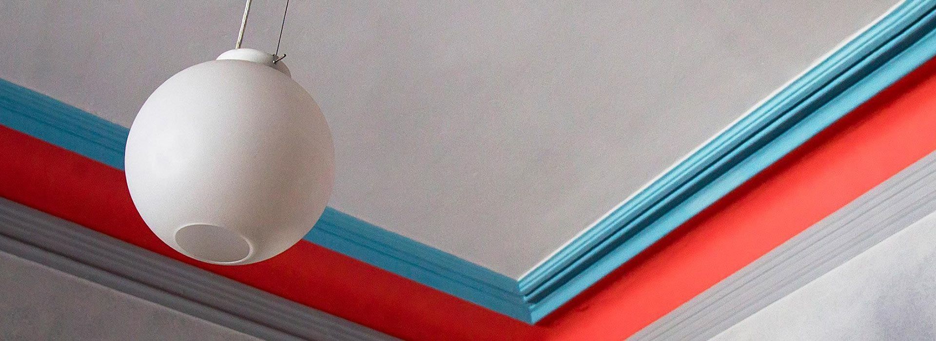 Valkoinen riippuvalaisin punaisen ja turkoosin kattolistan alla modernissa sisustuksessa